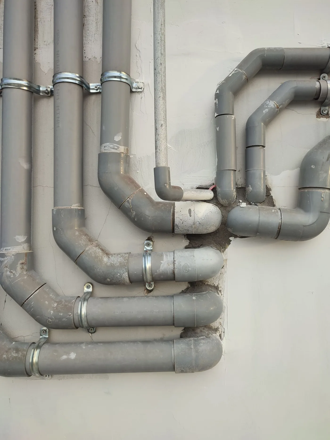 Réseau de canalisations PVC en applique sur un mur, coudes et colliers de fixation